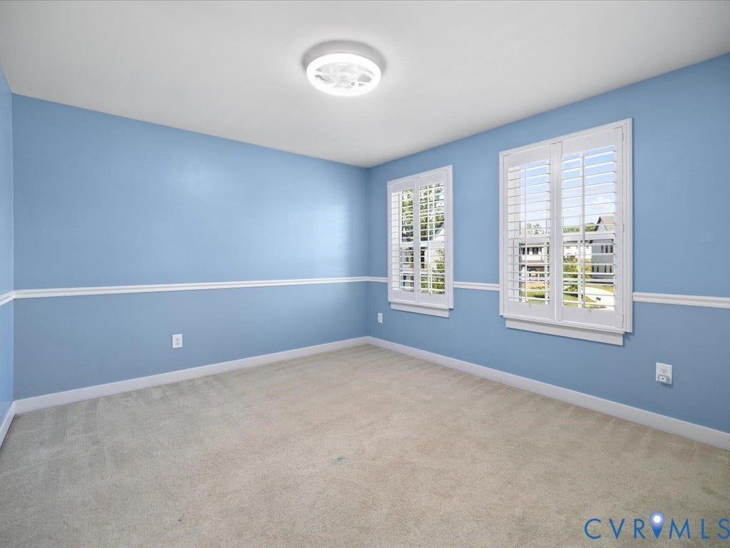 Plush carpeting, two windows with plantation shutters, light blue walls with chair rail molding, and a ceiling-mounted light fixture