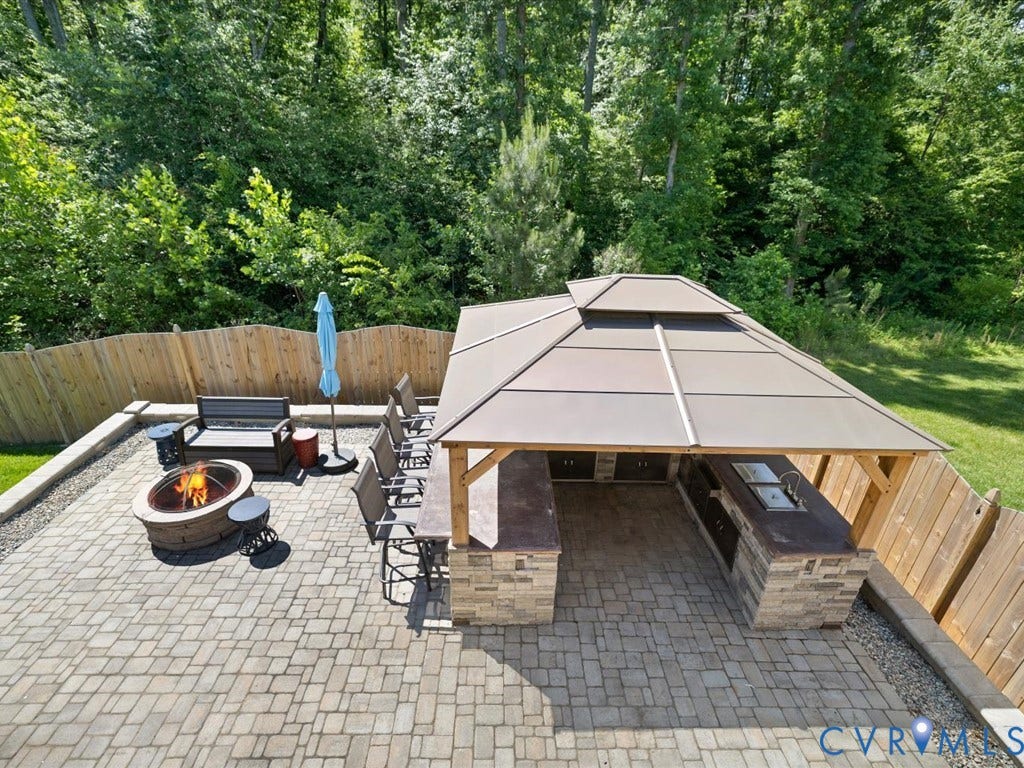 Paver patio featuring a built-in outdoor kitchen with sink, stone veneer accents, a permanent gazebo structure, and a fire pit
