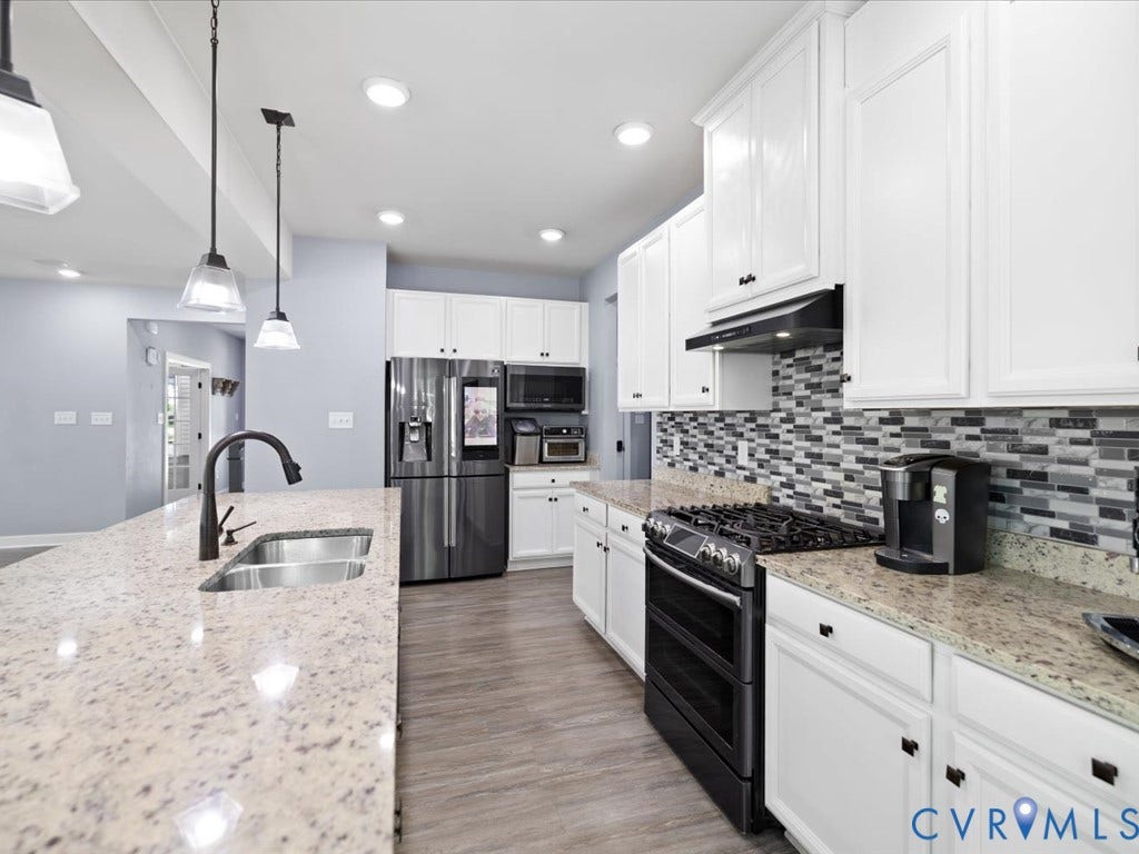 Kitchen featuring white cabinetry, light-toned countertops, a mosaic tile backsplash, stainless steel sink, and wood-finish flooring