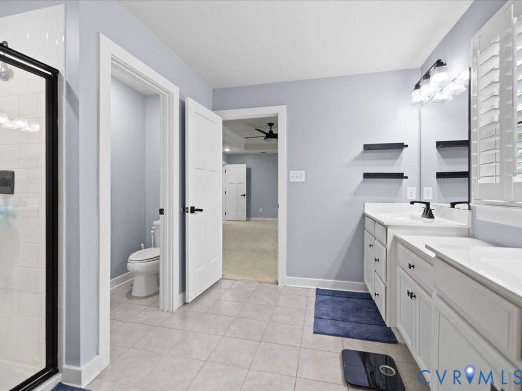 Bathroom featuring a dual-sink vanity with white countertops, a walk-in shower with a glass enclosure, tile flooring, and white panel doors