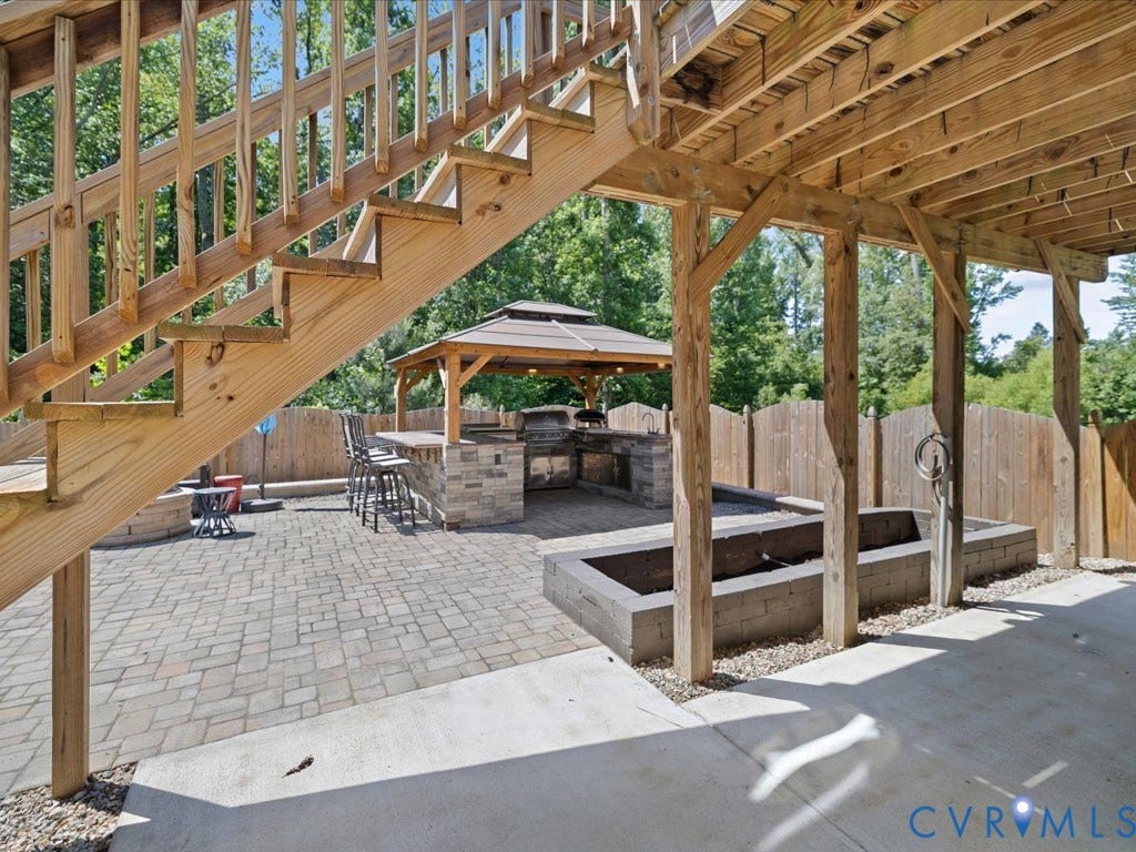 Outdoor entertaining space featuring a paver patio, stone-finish outdoor kitchen, and wooden privacy fence