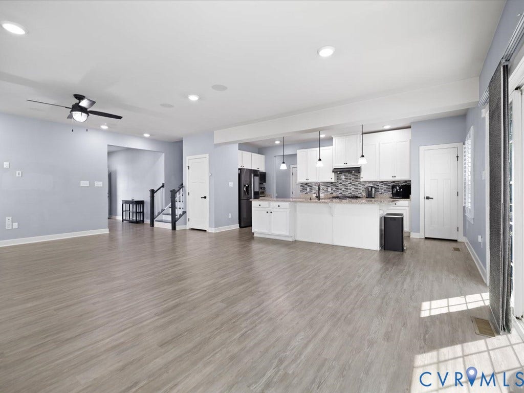 Open-concept living space featuring wood-finish flooring, recessed lighting, a modern ceiling fan, white kitchen cabinetry, and a patterned tile backsplash