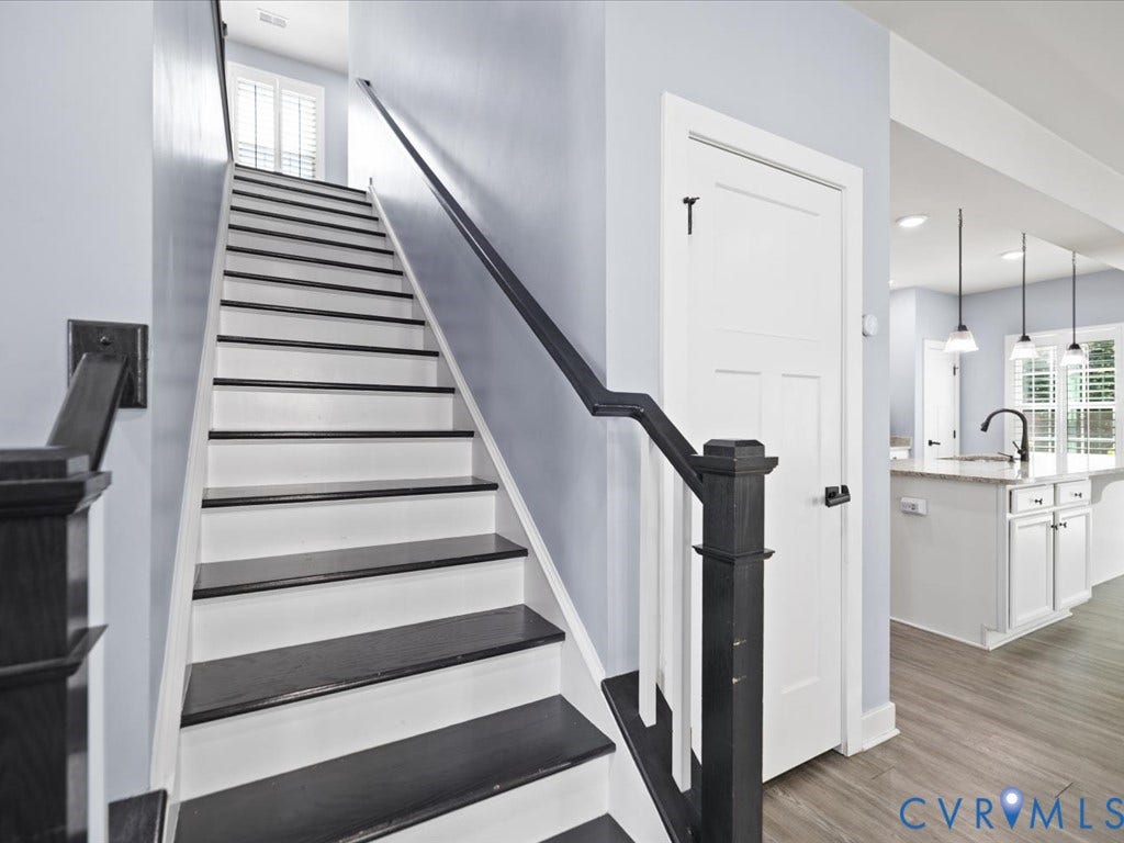 Two-tone staircase with contrasting risers and treads, wood-finish flooring, white panel door, and pendant lighting
