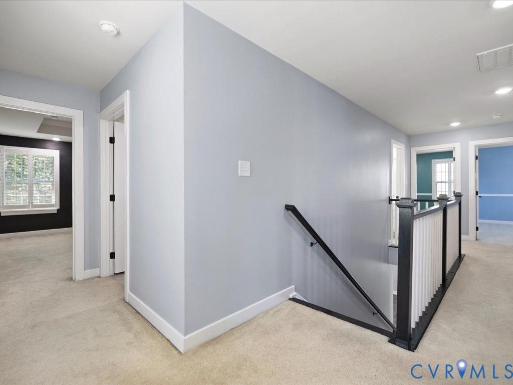 Neutral-toned carpeting throughout, contrasting interior doors, white trim details, recessed lighting, and a dark-finished stair railing with white balusters