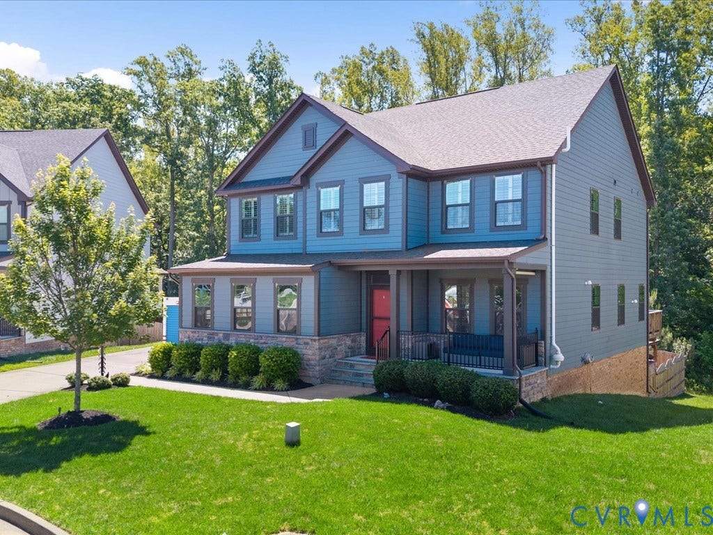 Two-story exterior with blue siding, stone accents, covered front porch, and a lush green lawn
