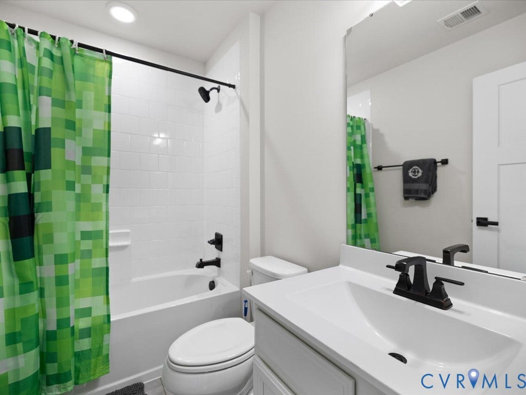 Built-in bathtub with subway tile surround, matte black fixtures, white vanity with integrated sink, and an unframed wall mirror
