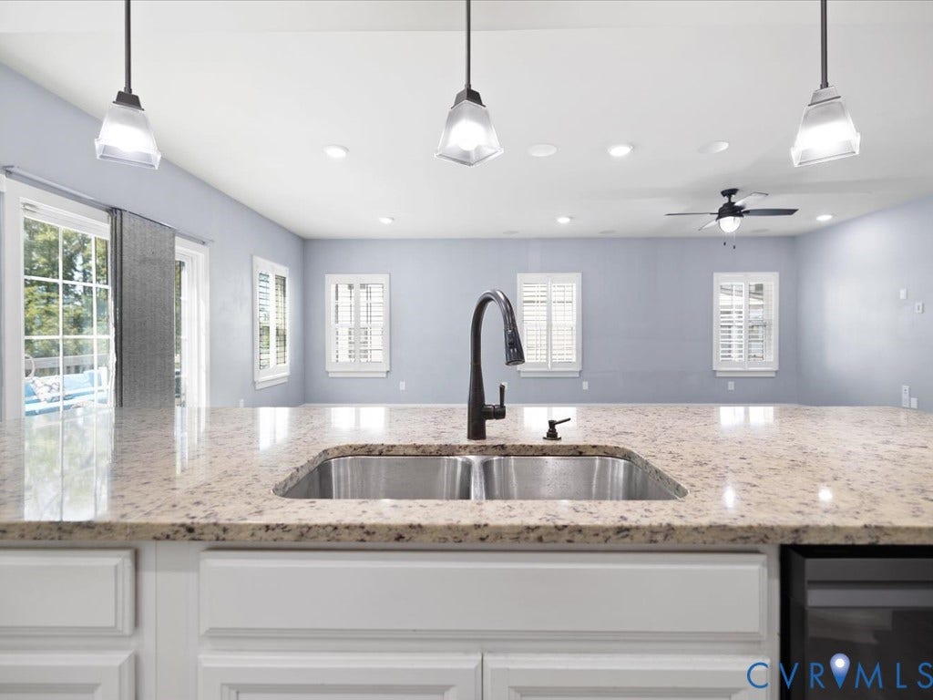 Kitchen island with a double basin stainless steel sink, dark bronze gooseneck faucet, light granite countertop, and recessed panel cabinetry