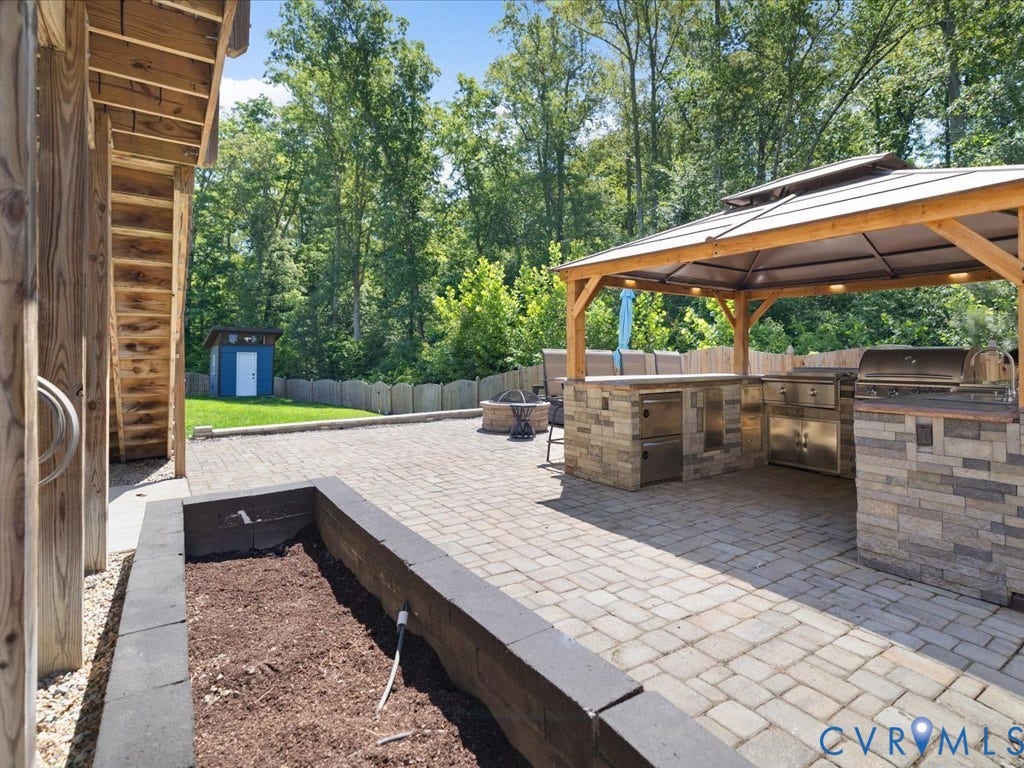 Paver patio featuring an outdoor kitchen with stainless steel appliances, stone veneer accents, and a built-in fire pit