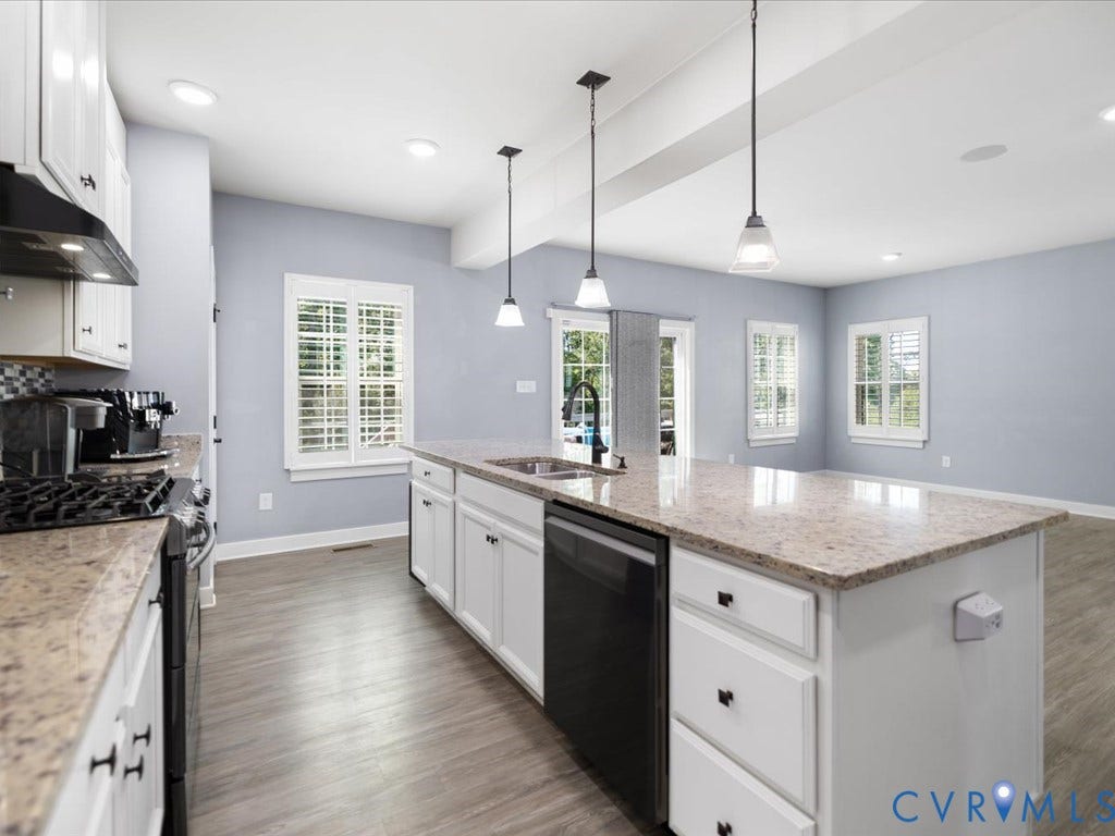 White cabinetry, light-toned countertops, wood-finish flooring, recessed lighting, and an island with pendant lights