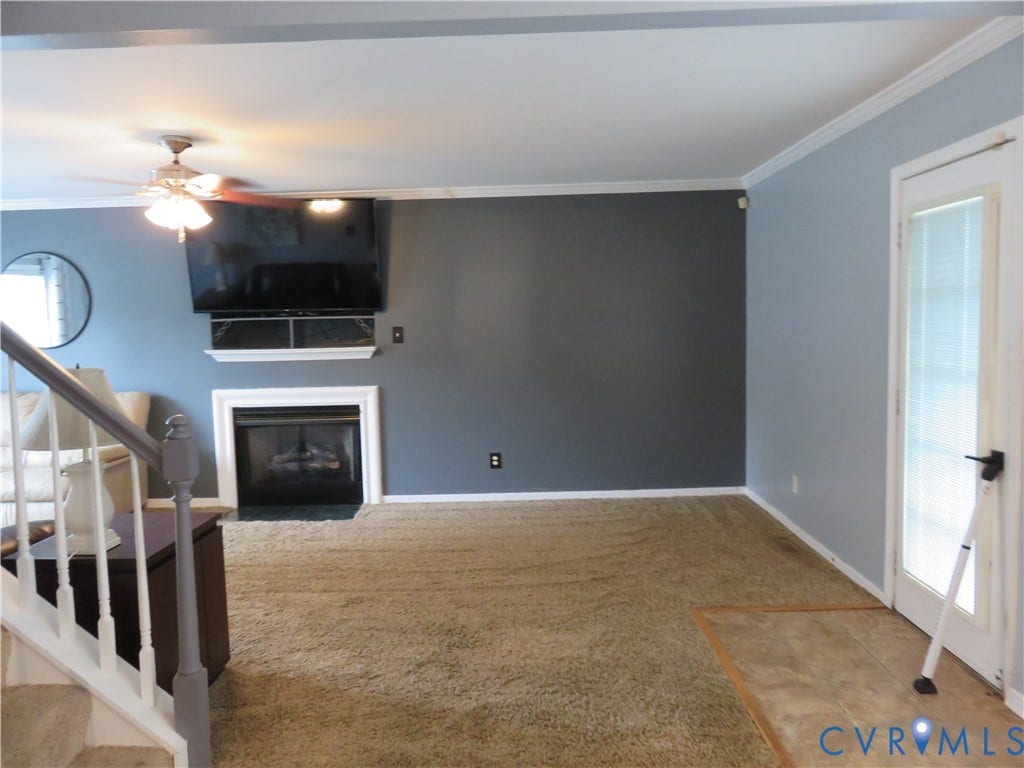 3107 McCabe Court, Chester, VA 23831 Spacious open-concept living area featuring wood-finish flooring, a fireplace with surround, wall-mounted flat-screen television, ceiling fan with integrated lighting, and direct access to exterior spaces via glass sliding doors