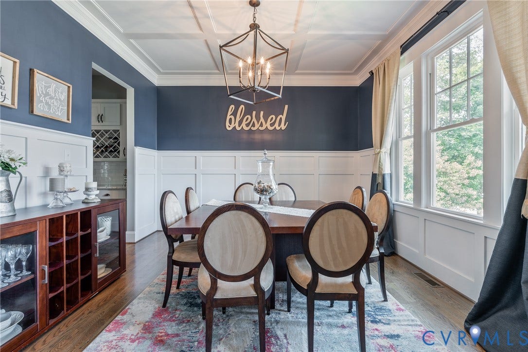 Coffered ceiling with a geometric chandelier, wood-finish flooring, wainscoting, and large windows with transom panels