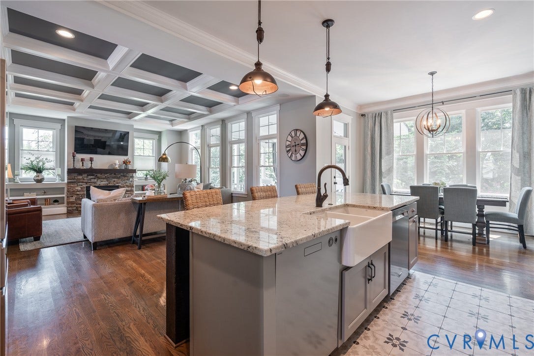 Open-concept living space with coffered ceilings, wood-finish flooring, and a stone-clad fireplace