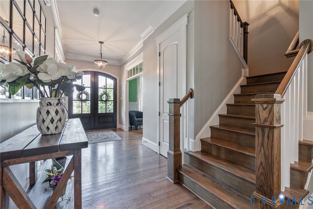 Hardwood flooring, wood-finish staircase with white balusters, transom window detailing, and an arched double-door entry
