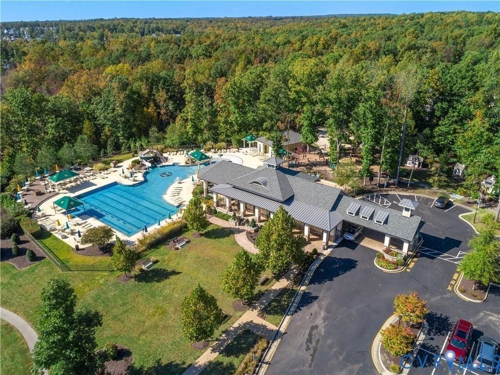 Community amenity building featuring a swimming pool, shaded pool deck, covered entry, and parking area