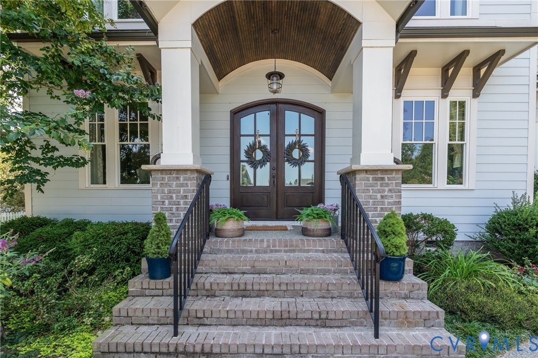 Brick staircase with wrought iron railings, double arch-top entry doors, wood-paneled arched portico ceiling, and light-toned siding