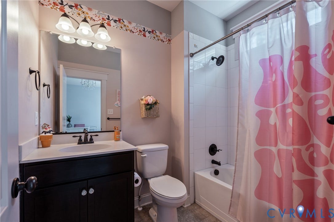 Bathroom featuring a white vanity countertop, dark wood-finish cabinetry, a built-in bathtub with white tile surround, and black plumbing fixtures