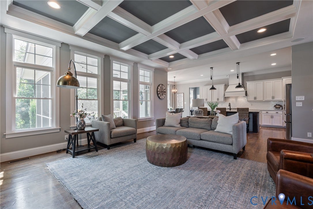 Expansive living area with wood-finish flooring, coffered ceiling, multiple windows, and recessed lighting