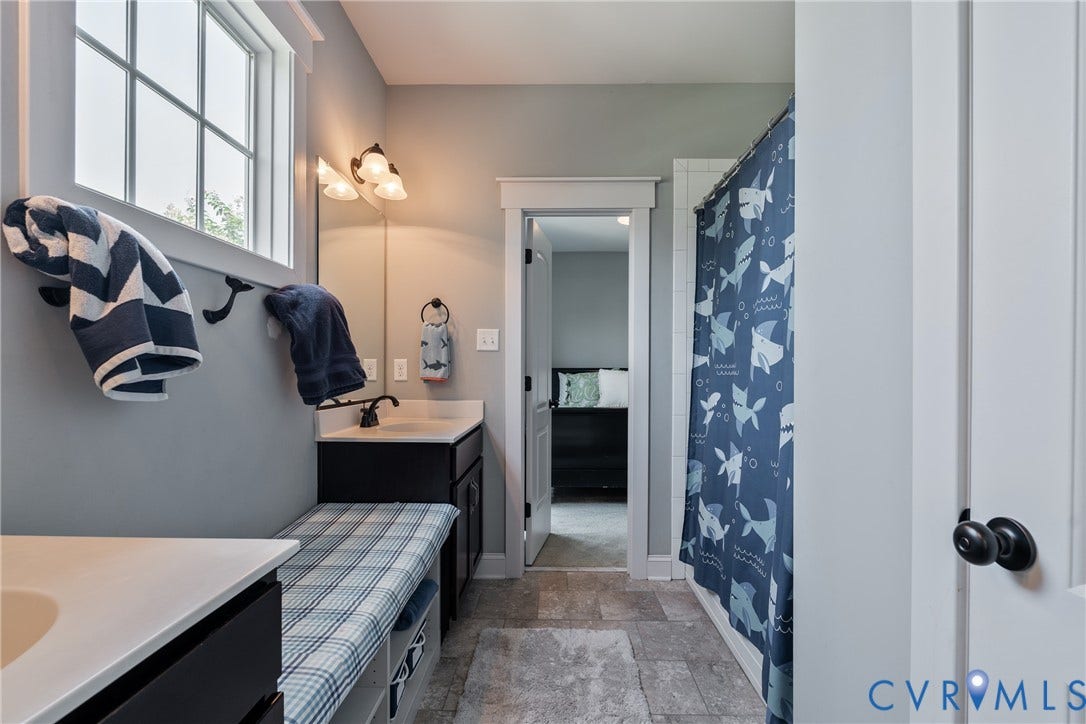 Window with white trim, built-in storage bench, single vanity with white countertop, wall-mounted light fixture, and tile flooring