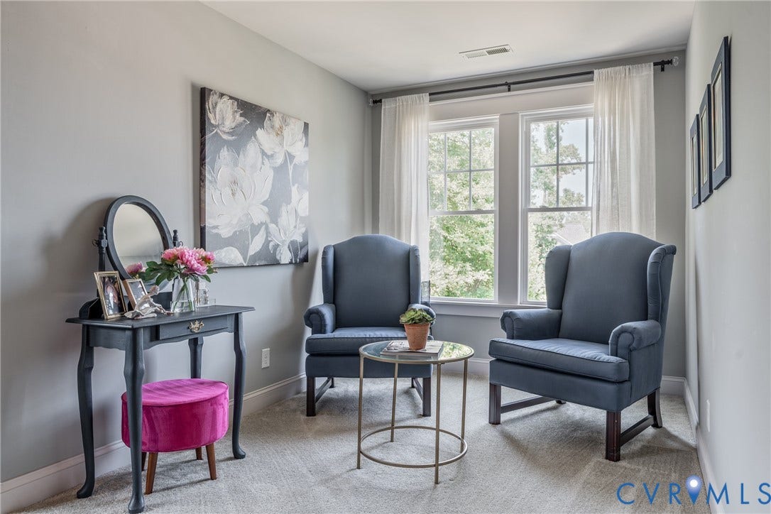 Double windows with white sheer curtains, neutral wall color, and light-colored carpet flooring