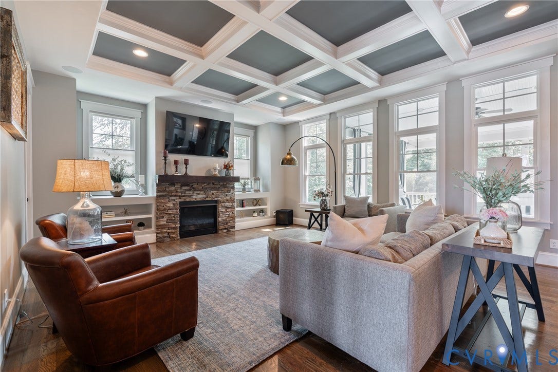 Coffered ceiling with recessed lighting, stone-clad fireplace with wood mantel, built-in shelving, hardwood flooring, and multiple large windows