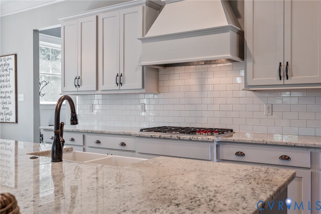 Kitchen featuring white shaker cabinets, speckled countertops, a gas range with a matching range hood, a subway tile backsplash, and a double basin sink with a dark bronze gooseneck faucet