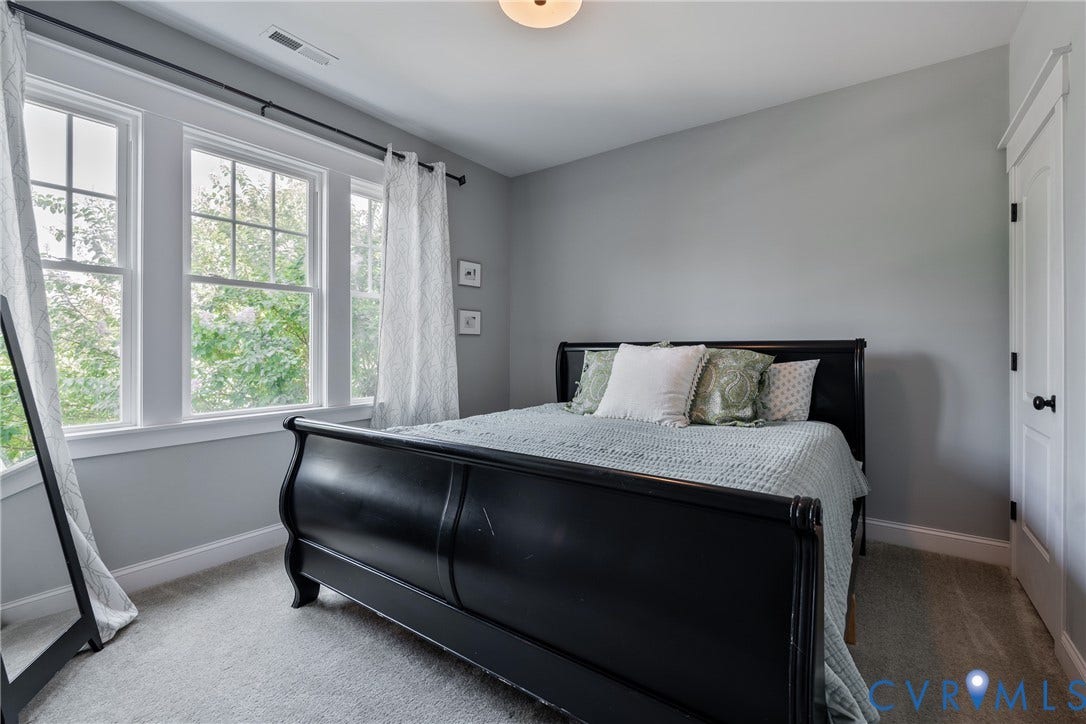 Light gray wall paint, carpeted flooring, built-in closet with white door and black hardware, triple window arrangement with white trim, and a flush-mount ceiling light
