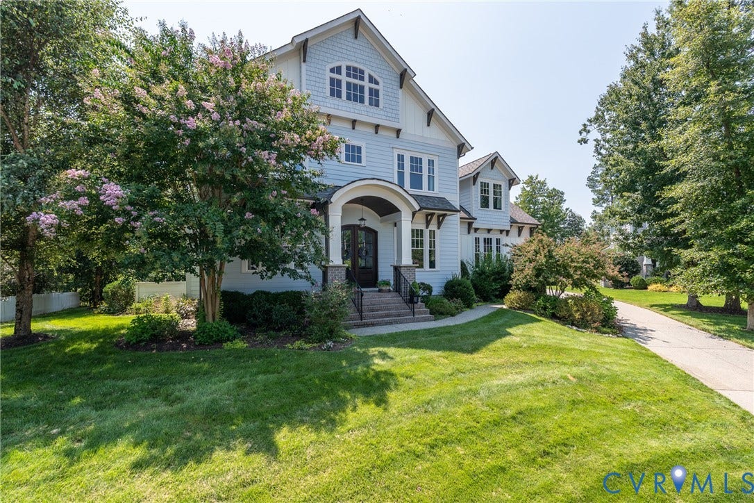 Light blue siding exterior, multiple gables, arched entry with stone accents, black entry door, and a paved driveway
