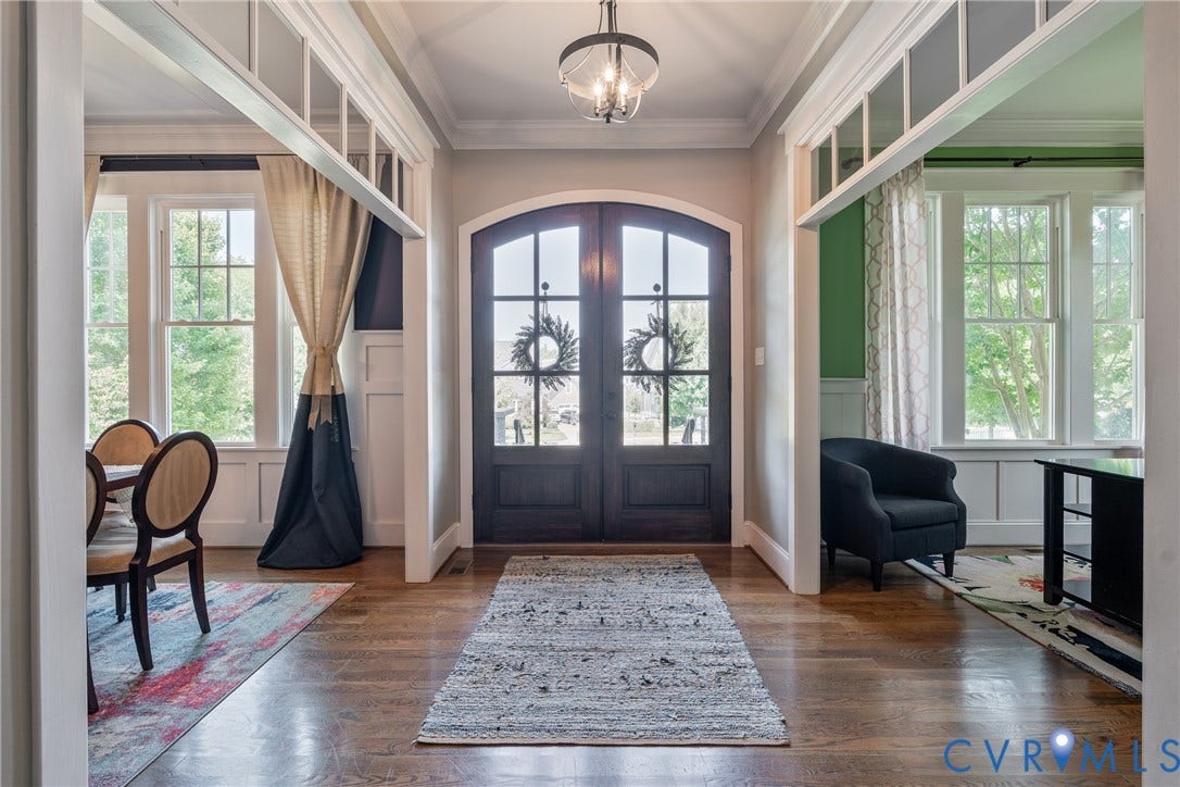 Arched double entry doors with glass panels, hardwood flooring, overhead semi-flush mount light fixture, and transom windows above architectural framing