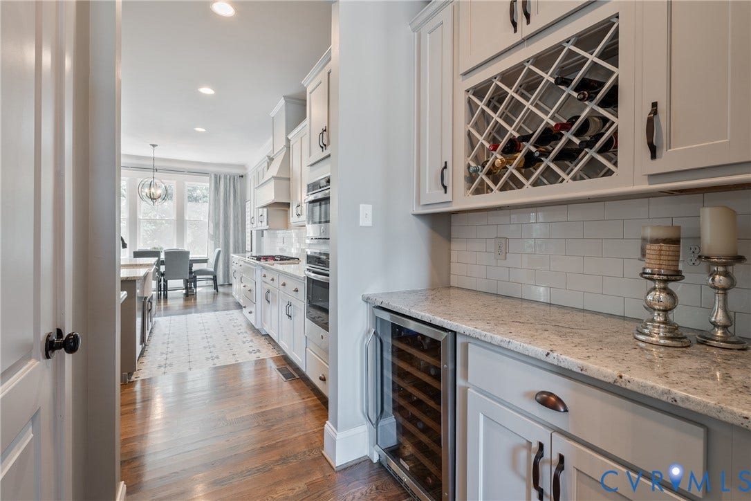 Wood-finish flooring, white cabinetry, integrated wine storage, white subway tile backsplash, and granite countertops
