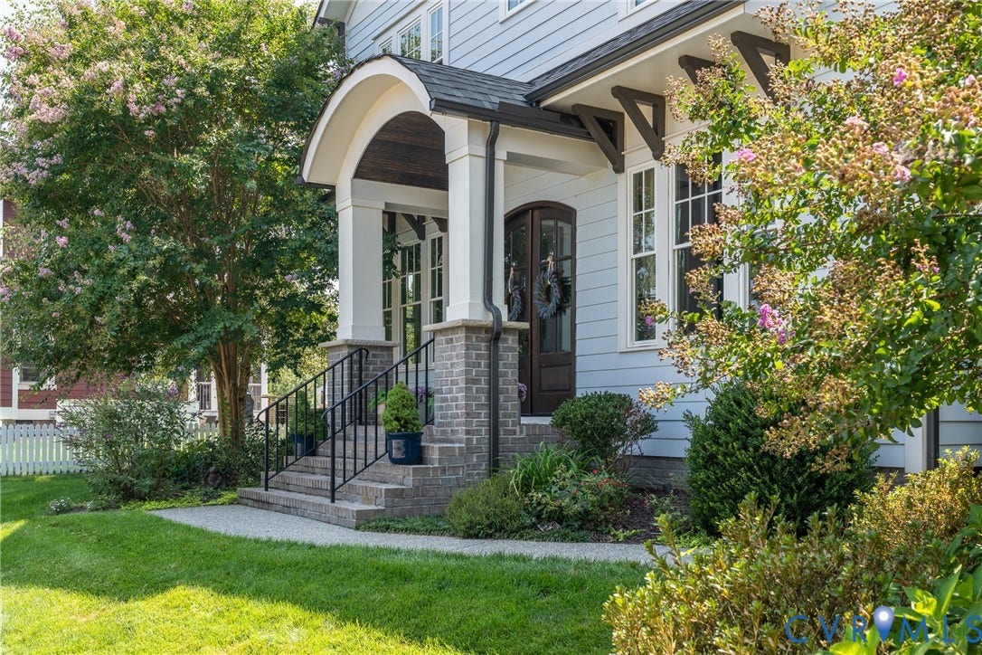 Light blue siding exterior with a covered entry, brick column bases, dark wood front door, and dark roof shingles