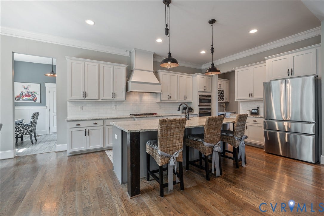 Spacious kitchen featuring wood-finish flooring, white cabinetry, a large island with an integrated sink, stainless steel appliances, and pendant lighting