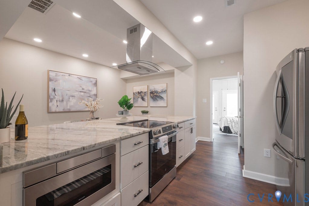 Kitchen featuring wood-finish flooring, stainless steel appliances, recessed lighting, white cabinetry, and a large central island with light-toned countertops
