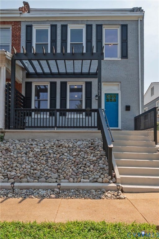 Stone faade with a vibrant blue entry door, featuring a front porch with a black pergola and railing