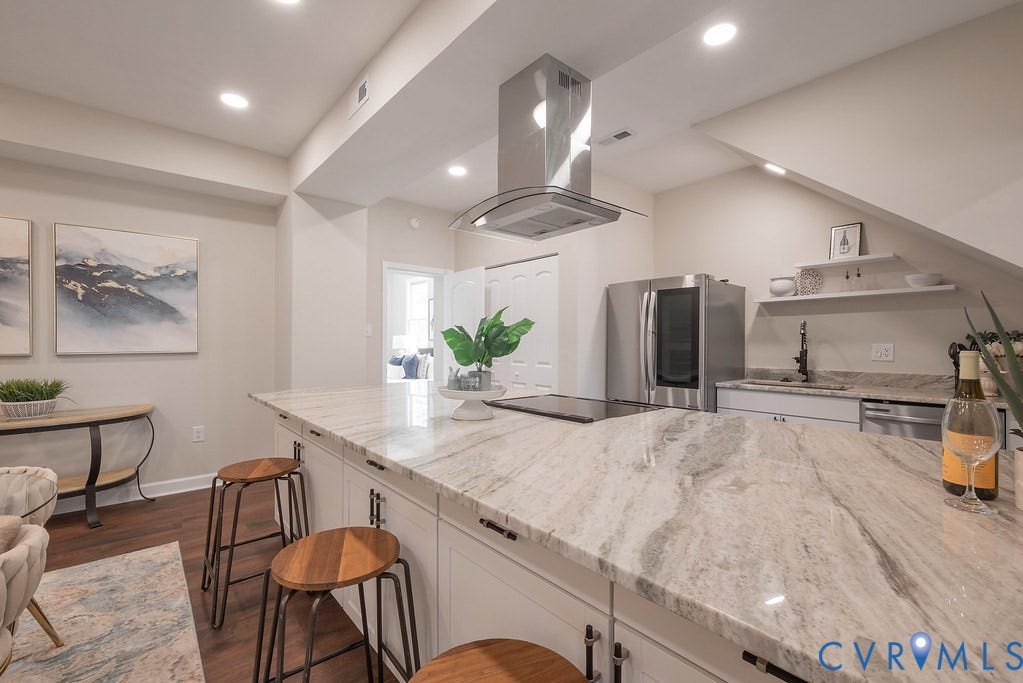 Kitchen island with a light-toned stone countertop, integrated cooktop, stainless steel range hood, and recessed lighting