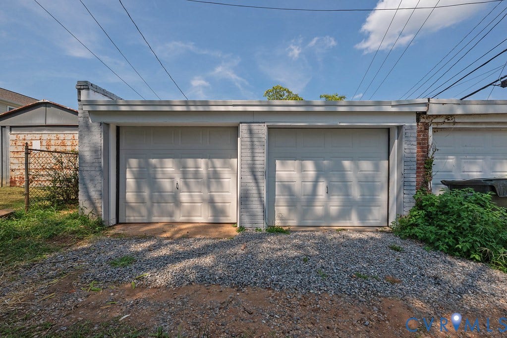 Two attached garage doors with paneling, set against a painted brick exterior, with a gravel surface approach