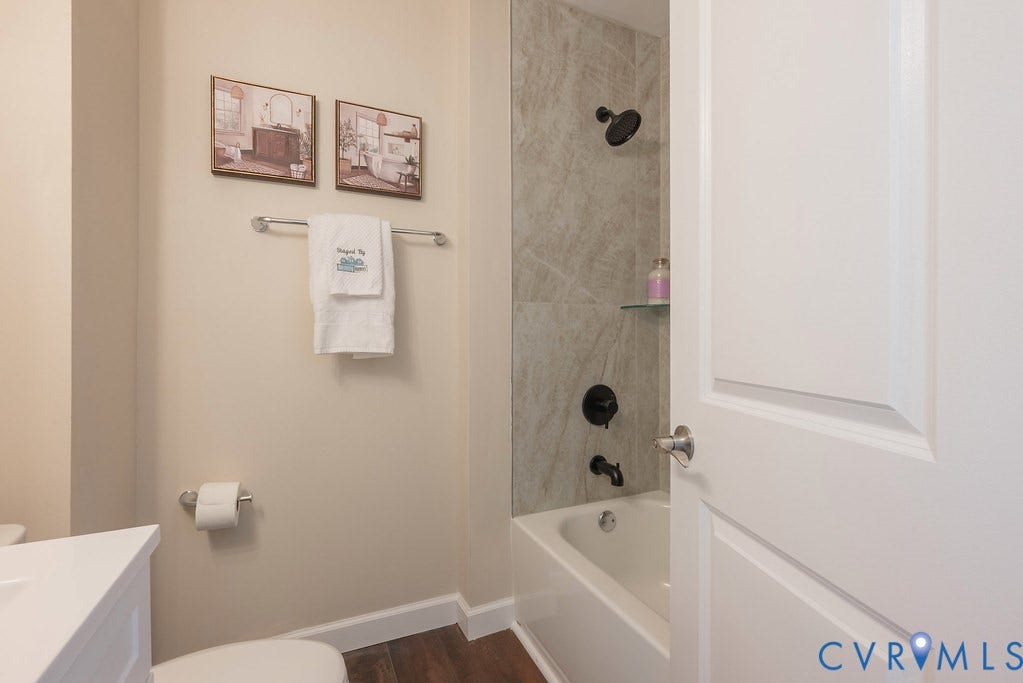 Bathtub with a tiled surround, matte black shower fixtures, and a clear glass shelf