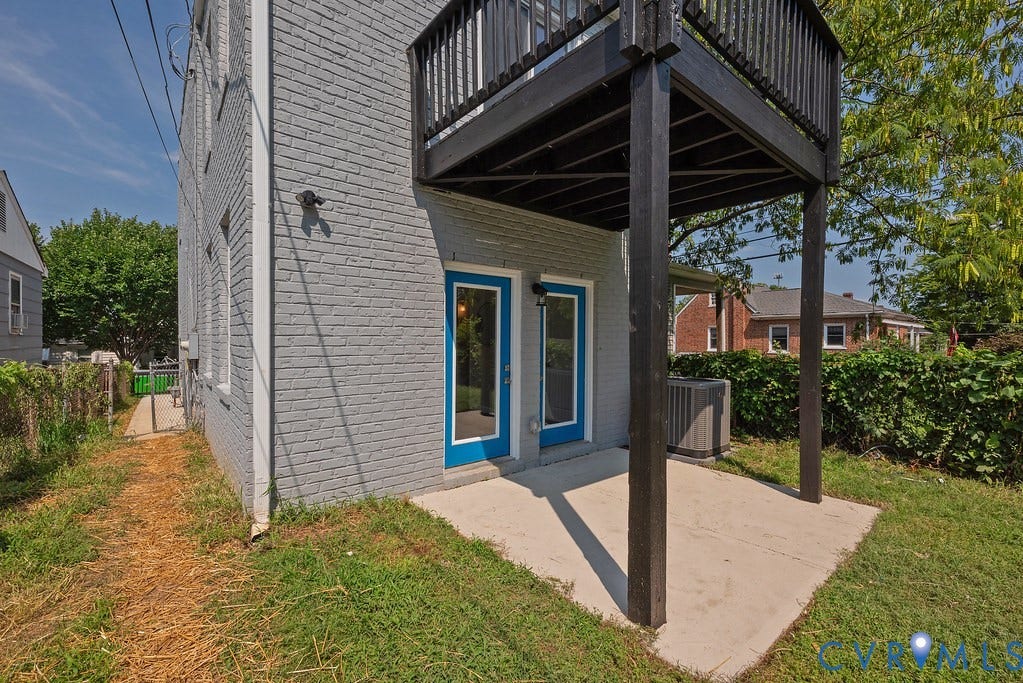 Rear exterior featuring a second-story balcony with wood railing, a ground-level patio, and two blue-framed glass doors