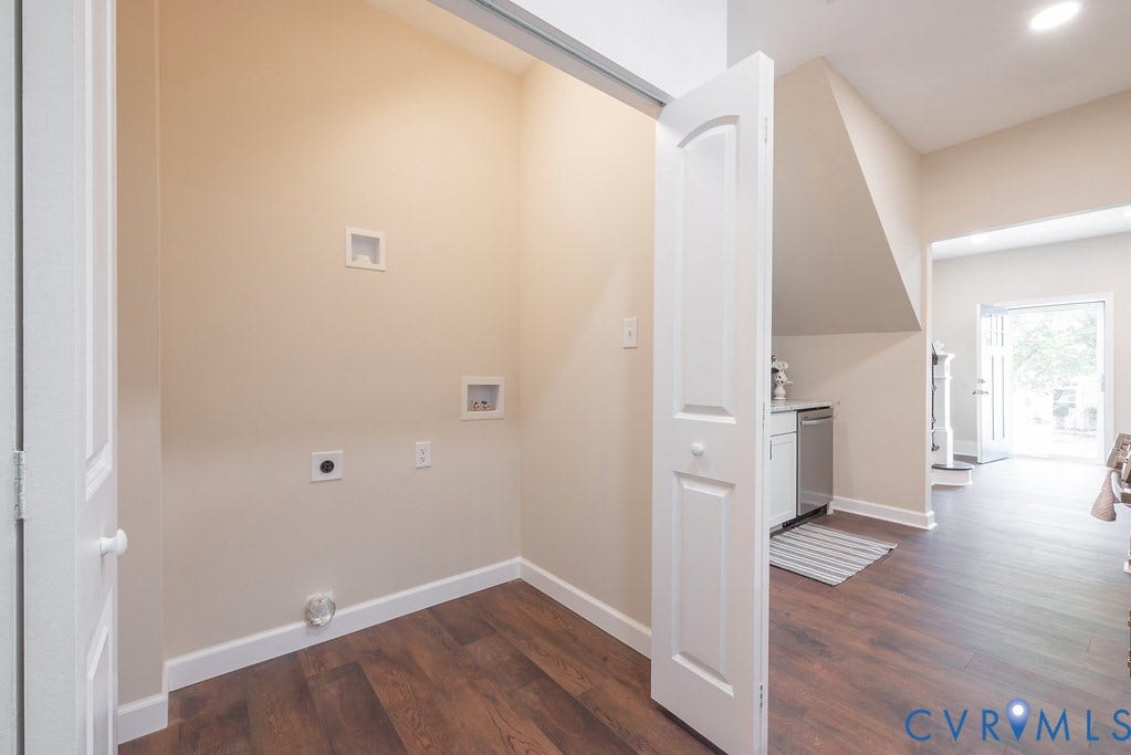 Laundry area with wood-finish flooring, white trim, and bi-fold door