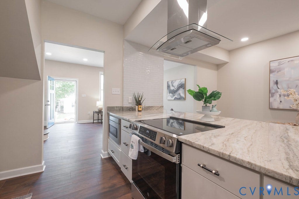 Kitchen featuring stainless steel appliances, a glass canopy range hood, wood-finish flooring, light-toned cabinetry, and a subway tile backsplash