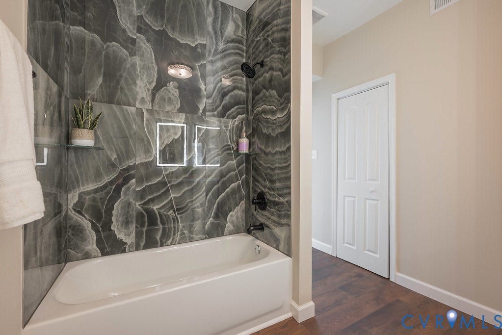 Bathtub with dark-toned marble-look tile surround, recessed lighting, and integrated shelving