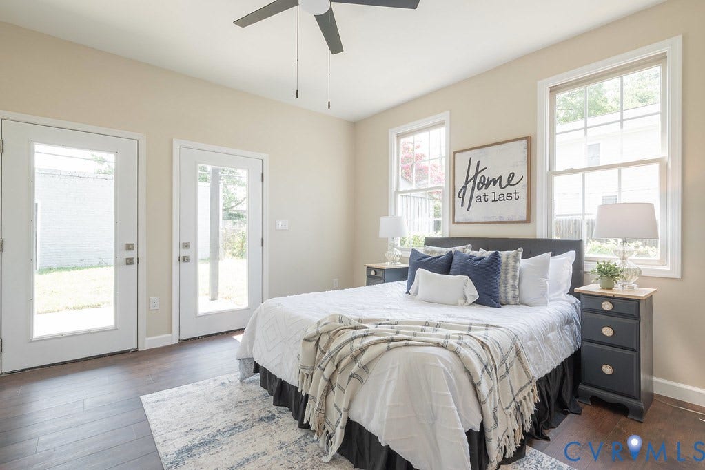 Wood-finish flooring, two glass-paneled doors, two large windows, a ceiling fan, and neutral wall tones