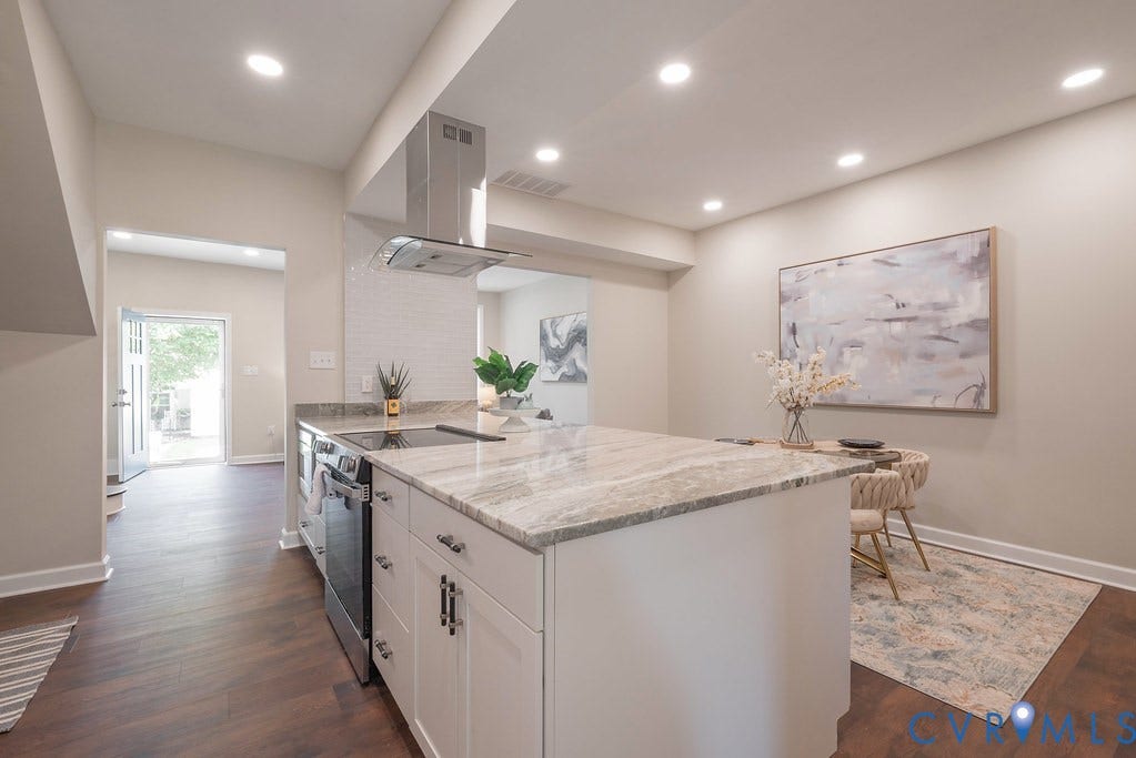 Kitchen featuring a large central island, light-toned countertops, white cabinetry with dark hardware, stainless steel range and hood, and wood-finish flooring