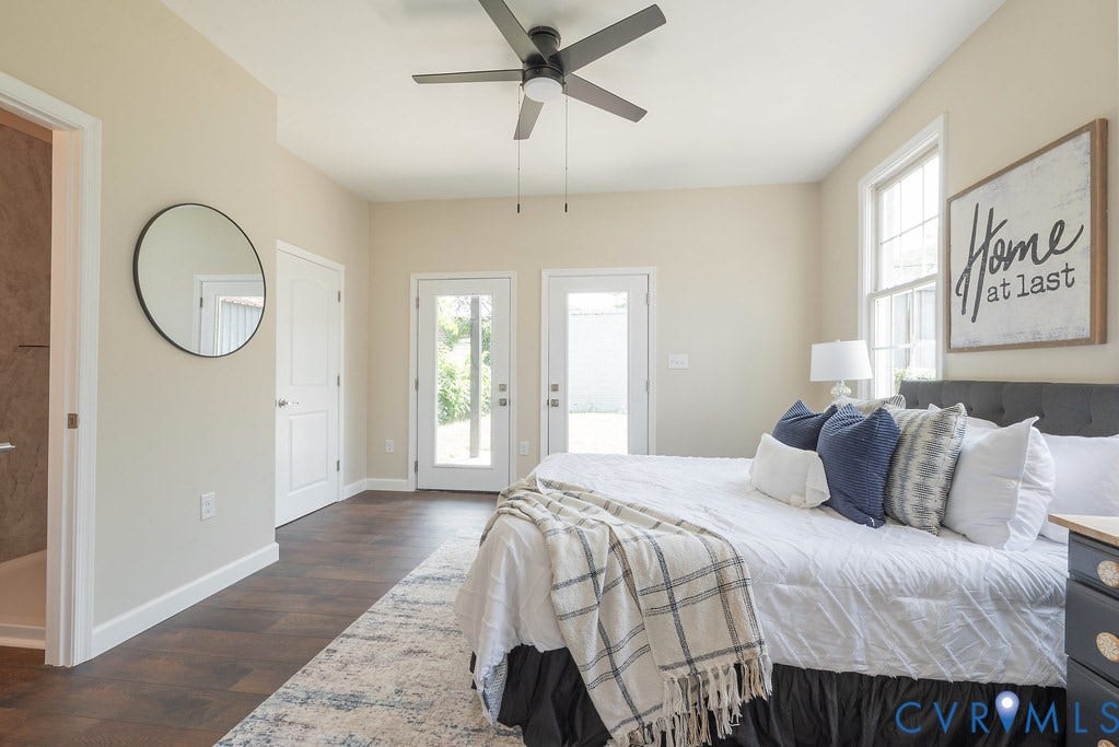 Wood-finish flooring, ceiling fan, two white doors, and a window with white trim