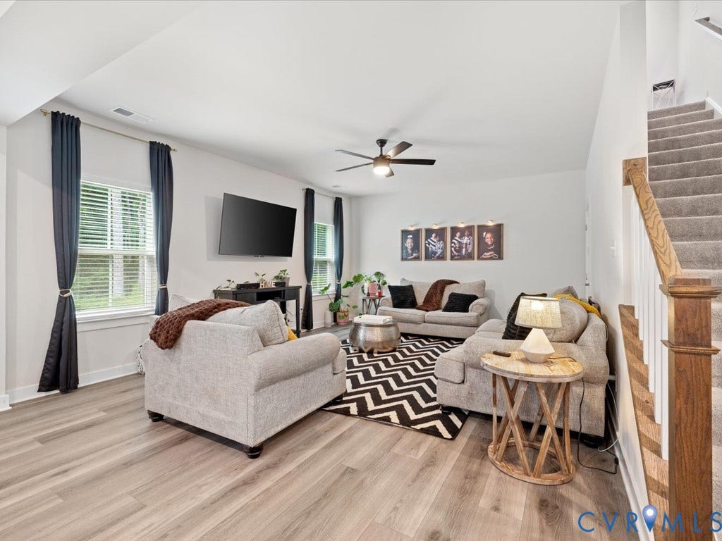 Expansive living area featuring light wood-finish flooring, a ceiling fan, and multiple windows