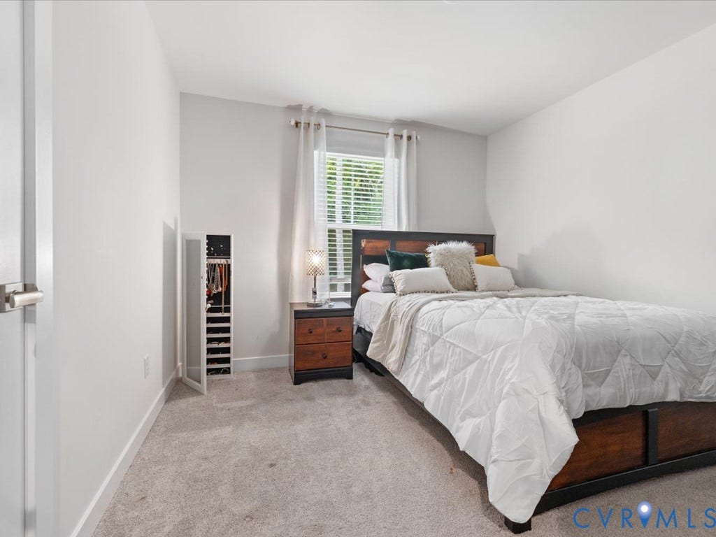 Light gray wall paint, light gray carpet flooring, window with blinds, white door with brushed nickel hardware