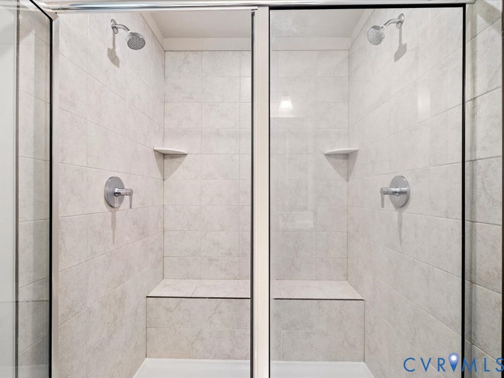 Dual shower stalls featuring full tile surrounds, built-in seating, integrated corner shelving, and glass enclosures