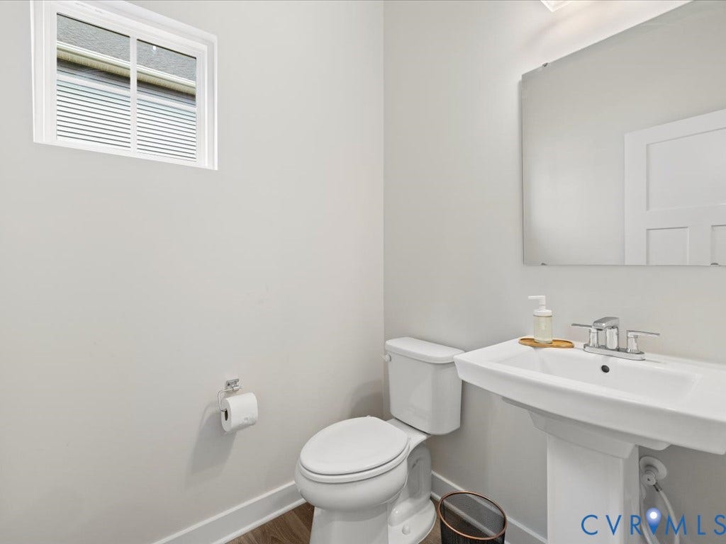 Pedestal sink with chrome faucet, white toilet, and wood-finish flooring