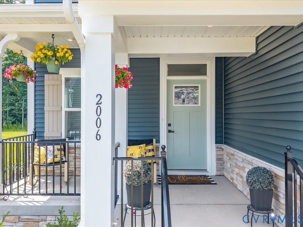 Front entrance featuring a light-colored door with decorative glass, dark blue siding, stone veneer accents, and a covered porch with metal railings