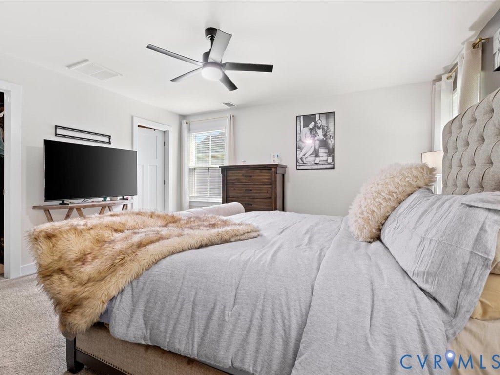 Ceiling fan with integrated lighting, window with blinds, light-colored walls, and neutral carpet flooring
