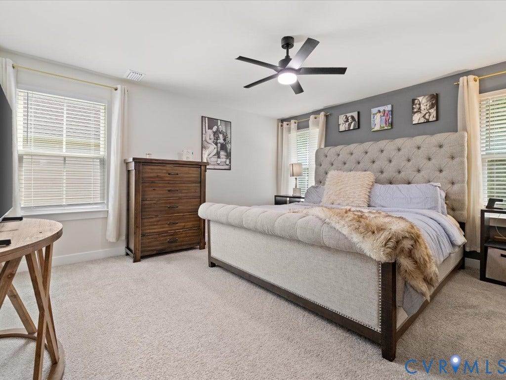 Light-colored carpeting, multiple windows with blinds, a ceiling fan with integrated lighting, and a dark accent wall